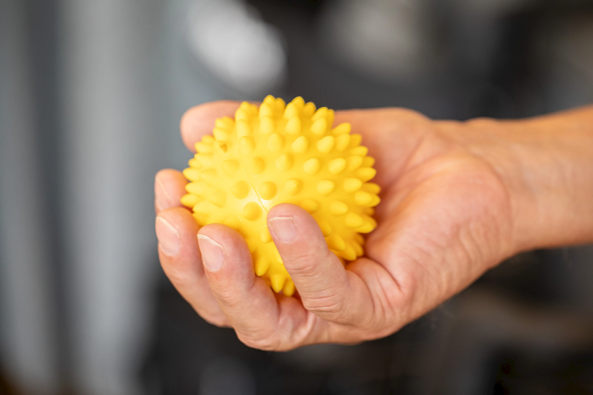 Hand h&auml;lt einen gelben Igelball zur Handtherapie